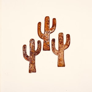 May include: Three rusty metal cactus cutouts in the shape of saguaro cacti. The cutouts are arranged in a triangular shape.