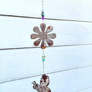 May include: A rusty metal wind chime with a butterfly, flower, and bee design. The chime has colorful beads and a bell at the bottom.