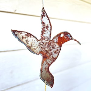 May include: A rusty metal hummingbird wind chime with a gold chain and beads. The hummingbird is in flight with its wings spread out.