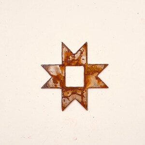 May include: A rusty metal star with a square hole in the center. The star is a traditional Native American design.