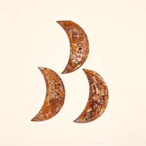 May include: Three rusty metal crescent moon shapes on a white background.