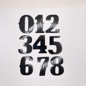 May include: Black vinyl numbers 0 through 8, with a glossy finish. The numbers are arranged in three rows, with the first row containing 0, 1, and 2, the second row containing 3, 4, and 5, and the third row containing 6, 7, and 8.