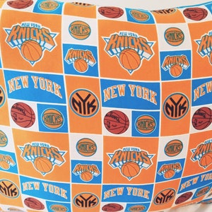 May include: Orange and blue fabric with a repeating pattern of the New York Knicks logo, basketballs, and the words "New York Knicks".