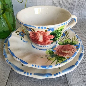 May include: A vintage teacup and saucer set with a floral design. The cup and saucer are white with blue and green accents. The floral design features pink roses and green leaves.