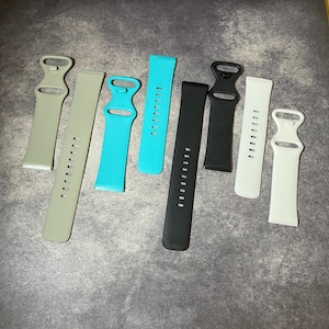 May include: Eight different colored watch bands, including gray, blue, black, and white. The bands are made of a soft, flexible material and have a buckle closure.