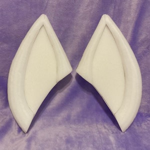 May include: Two white foam ear shapes for crafting. The ears are flat and have a curved shape.