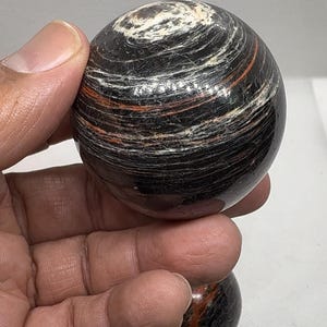 May include: Two black and red striped spheres made of polished stone. The spheres are smooth and have a swirling pattern.