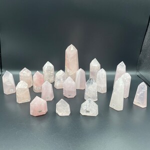 May include: A collection of 16 rose quartz crystal points, some are polished and some are raw, all are a light pink color.