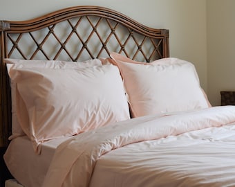 May include: A bed with a woven rattan headboard and a light pink duvet cover and two matching pillowcases.