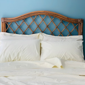 May include: A white bed with a woven rattan headboard and two white pillows. The bed is made with crisp white linens.
