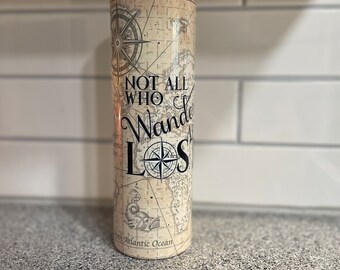 May include: A stainless steel tumbler with a black lid and a map design. The tumbler features the text "Not all who wander are lost" and a compass.
