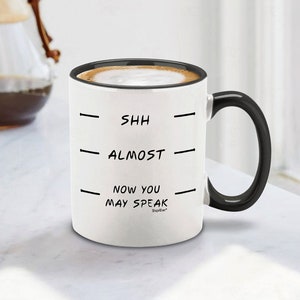May include: White ceramic coffee mug with a black handle. The mug has black text that reads "Shh - Almost - Now You May Speak - Shop4Ever".
