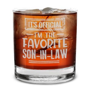May include: A clear glass tumbler with a brown liquid inside. The glass has the text "It's Official - I'm the Favorite Son-in-Law" etched on the side.