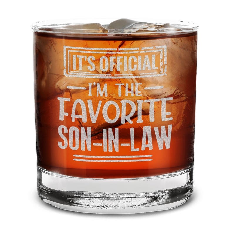 May include: A clear glass tumbler with a brown liquid inside. The glass has the text "It's Official - I'm the Favorite Son-in-Law" etched on the side.