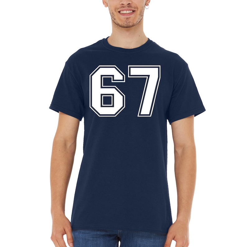 May include: Navy blue t-shirt with the number 67 in white, outlined in navy. The number is large and centered on the shirt. The shirt is a crew neck style.