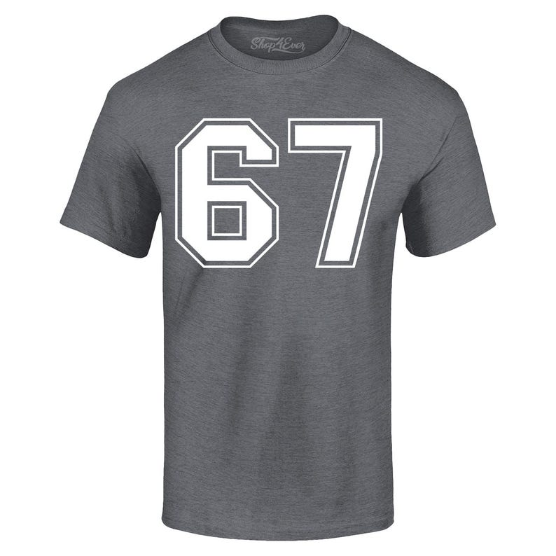 May include: A gray short-sleeve t-shirt with the number "67" in white block letters. The number is outlined in white. The shirt has a crew neck and the brand name "Shop4Ever" is printed on the collar.
