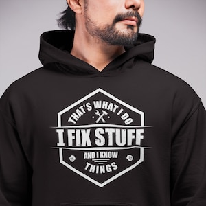 May include: Black hoodie with a white graphic design that says "That's what I do I fix stuff and I know things". The graphic is a hexagon with a wrench and screwdriver inside.