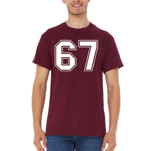 May include: Maroon t-shirt with the number 67 in white, outlined in white. The number is in a collegiate font. The shirt is short-sleeved and made of a soft material.