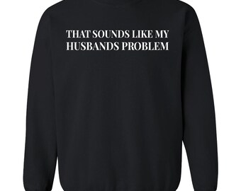 Może przedstawiać: Czarna bluza z okrągłym dekoltem z białym napisem "THAT SOUNDS LIKE MY HUSBANDS PROBLEM". Bluza ma długie rękawy i prążkowany kołnierz. Logo Shop4Ever jest widoczne u góry.