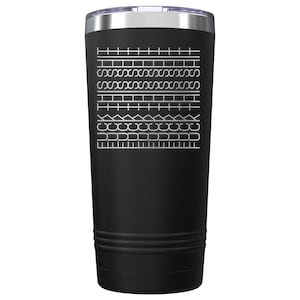 Könnte beinhalten: Schwarzer isolierter Becher mit silbernem Rand und Deckel. Der Becher hat ein weißes geometrisches Design aus verschiedenen Formen und Linien. Das Design ist in die schwarze Oberfläche geätzt und erzeugt einen visuellen Kontrast.