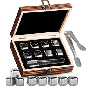 Op de afbeelding: Een houten kistset met whisky stenen en tangen van roestvrij staal. De kist is open en onthult de stenen gerangschikt in een zwart fluwelen interieur. Elke steen is gegraveerd met de letters "CSL".