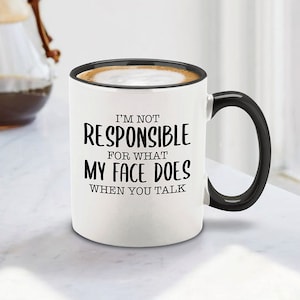 Könnte beinhalten: Eine weiße Keramik-Kaffeetasse mit schwarzem Henkel. Die Tasse hat einen schwarzen Text mit der Aufschrift "Ich bin nicht verantwortlich für das, was mein Gesicht tut, wenn du sprichst."
