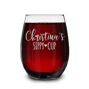 May include: A clear glass wine glass with a red wine inside. The glass has the text "Christina's Sippy Cup" etched on the side.