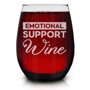 May include: A stemless wine glass with the text "Emotional Support Wine" etched on the side. The glass is filled with red wine.