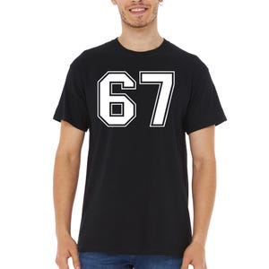 May include: Black t-shirt with the number 67 in white, outlined in black. The number is in a bold, collegiate-style font. The shirt is a crew neck style.