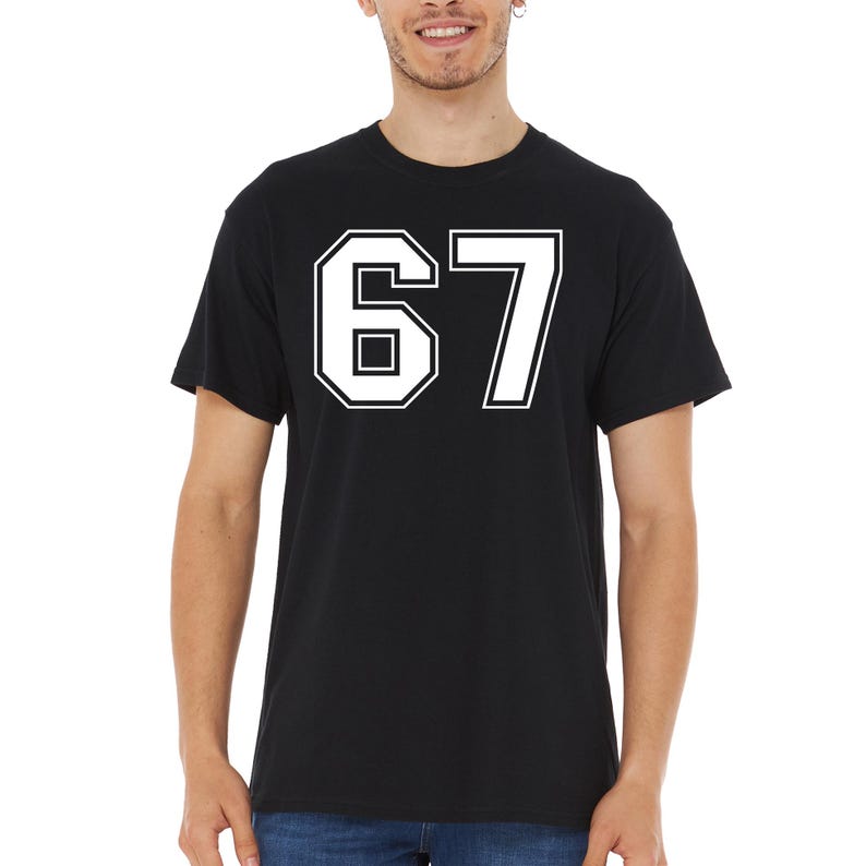 May include: Black t-shirt with the number 67 in white, outlined in black. The number is in a bold, collegiate-style font. The shirt is a crew neck style.