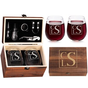 Op de afbeelding: Een houten wijngeschenkset met twee stamloze wijnglazen gevuld met rode wijn, een houten kist en wijnaccessoires. De glazen en de kist hebben de initialen "CSL". De kist is van donker hout.