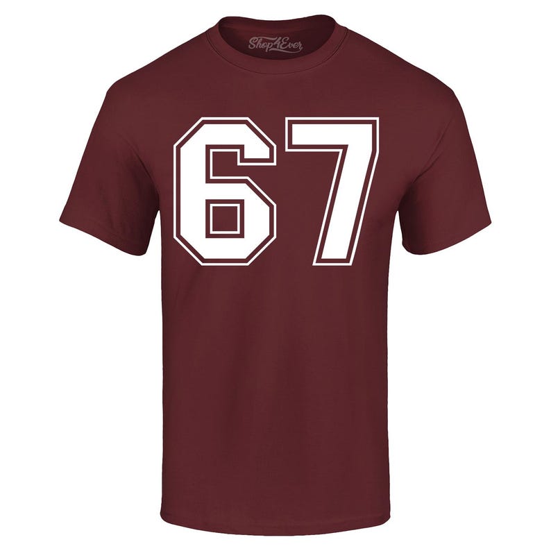May include: A maroon t-shirt with the number "67" in white, outlined in white. The number is large and centered on the front of the shirt. The shirt has short sleeves and a crew neck. The brand name "Shop4Ever" is printed on the top.