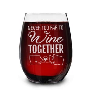 Op de afbeelding: Een stamloze wijnglas gevuld met rode vloeistof. Op het glas staat de gegraveerde tekst "NEVER TOO FAR TO Wine TOGETHER", samen met twee staatscontouren verbonden door een hart. Het glas is helder.