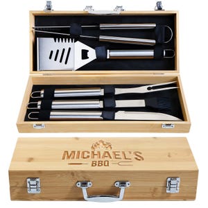 May include: A barbecue tool set in a wooden case, featuring stainless steel utensils. The set includes a spatula, fork, knife, basting brush, and tongs. The case is engraved with "MICHAEL'S BBQ" and secured with metal latches.