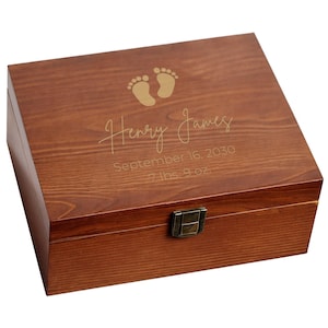 May include: A wooden keepsake box with a hinged lid. The lid is engraved with baby footprints, the name "Henry James", the birth date "September 16, 2030", and the birth weight "7 lbs. 9 oz.". The box has a dark brown finish and a metal clasp.