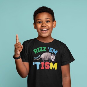 May include: A black t-shirt with a colorful graphic of a possum and the text "Rizz 'em with the 'Tism" printed on the front.