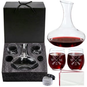 Op de afbeelding: Een wijnkarafset in een zwarte geschenkdoos. De set bevat een heldere glazen karaf, twee stamloze wijnglazen en twee kleinere glazen. De wijnglazen zijn gevuld met rode wijn en hebben een gepersonaliseerd ontwerp.