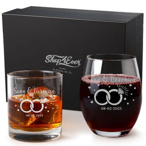 May include: Two engraved wedding glasses, one with amber liquid and ice, the other with red liquid. Both glasses display the names "Sean & Veronica", interlocking rings, a diamond, hearts, and the date "08-02-2025". A black gift box is visible in the background.