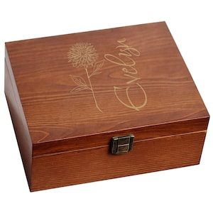May include: A wooden box with a hinged lid and a metal clasp. The box is stained a warm brown color and features an engraved floral design and the name "Evelyn" in a cursive font on the lid.