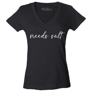 May include: Black V-neck t-shirt with the phrase "needs salt" in white script. The shirt has short sleeves and a classic fit. The brand name "Shop4Ever" is printed at the top of the shirt.