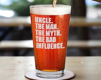 May include: A clear glass pint glass with the text "UNCLE. THE MAN. THE MYTH. THE BAD INFLUENCE." printed on the side. The glass is filled with a reddish-brown liquid.