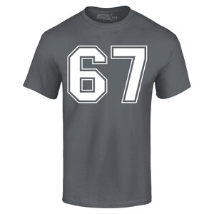 May include: A charcoal gray t-shirt with the number "67" in white block lettering. The number is outlined in white, with a white border. The shirt has short sleeves and a crew neck.