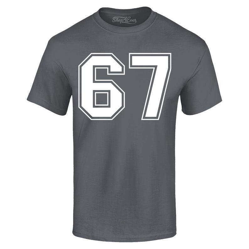 May include: A charcoal gray t-shirt with the number "67" in white block lettering. The number is outlined in white, with a white border. The shirt has short sleeves and a crew neck.
