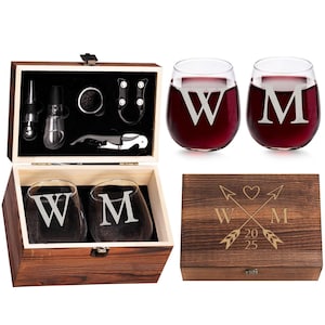 Op de afbeelding: Een houten wijngeschenkset met twee stamloze wijnglazen met de letters "W" en "M" gegraveerd. De set bevat een houten kist met wijnaccessoires en een deksel met gegraveerde pijlen, een hart en de letters "W" en "M".