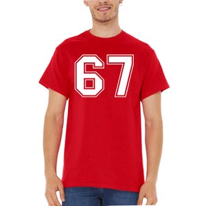 May include: A red t-shirt with the number 67 in white, outlined in a thicker white border. The shirt is a classic crew neck style.