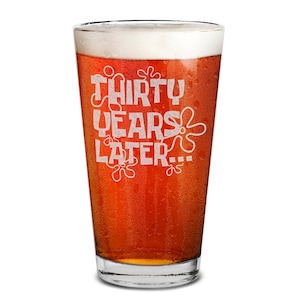 May include: A pint glass filled with a light amber liquid and topped with a foamy head. The glass features the text "THIRTY YEARS LATER..." in a white, playful font, with decorative sponge-like shapes.