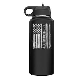 May include: Black stainless steel water bottle with a black lid and a carrying handle. The bottle has a distressed American flag design with the text "BEST HUSBAND EVER" printed vertically on the right side of the flag.