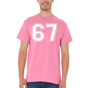 May include: A pink t-shirt with the number 67 in white, featuring a bold, outlined font. The shirt is a solid color, with a crew neck and short sleeves. The number is centered on the chest.