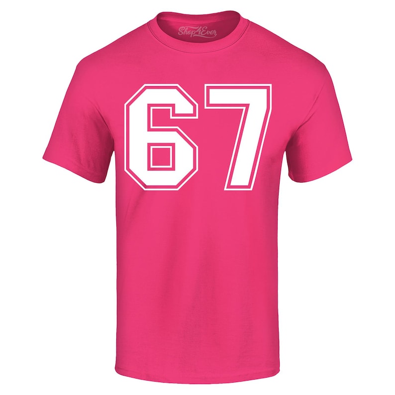 May include: A bright pink t-shirt with the number "67" printed in white block letters. The number is outlined in white. The shirt has short sleeves and a crew neck.