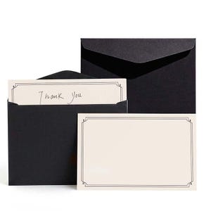 May include: A set of black envelopes with matching cream-colored cards. One card has the handwritten text "Thank You" inside a decorative border. The other card is blank with a similar border. The envelopes are closed.